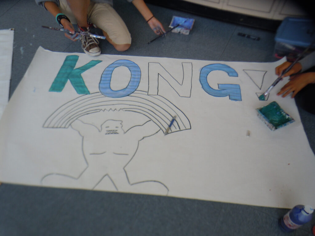 Students kneeling on the floor painting "KONG!" the Rooftop mascot for a sign celebrating Rooftop's 40th Birthday in 2012.