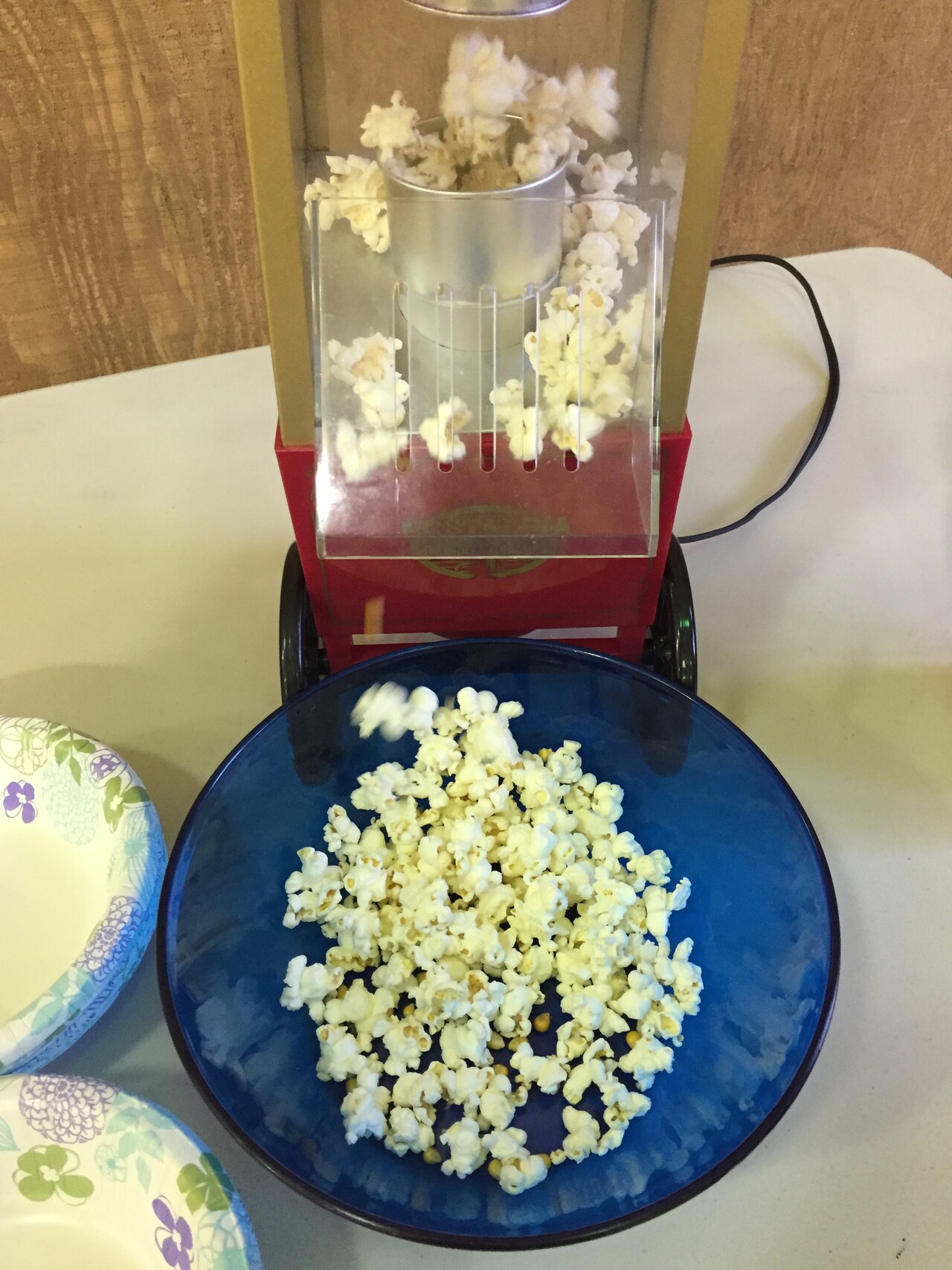 A blue bowl catches the hot popcorn as it falls from the red air popper at Mayeda Movie Night.